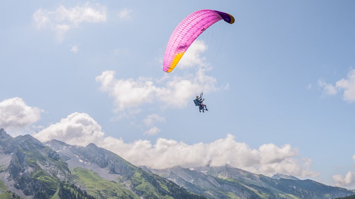 Experience the thrill of paragliding over the stunning Alps on a bright day.